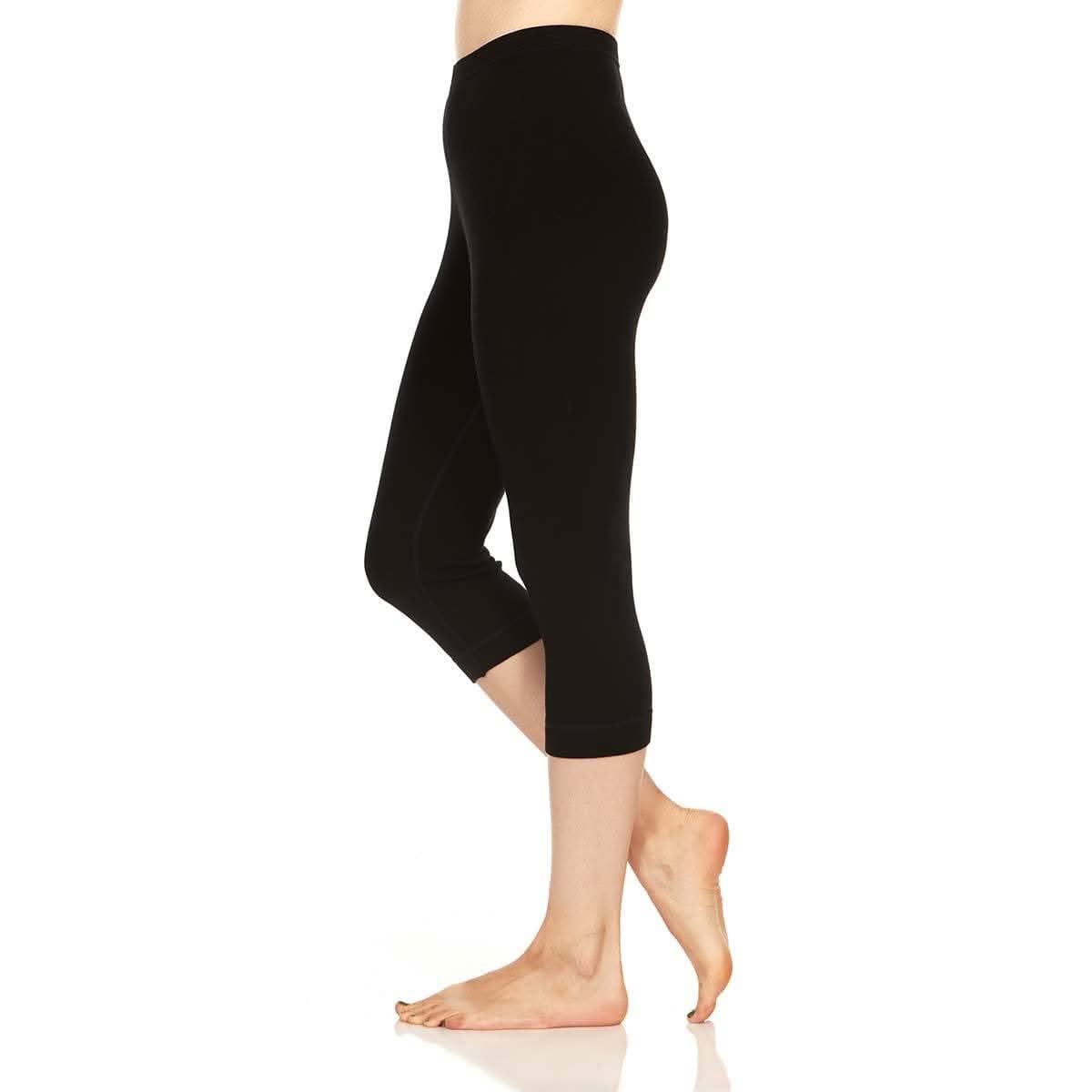 Right side view from waist to feet of a woman wearing black Osceola midweight merino wool three-quarter base-layer bottoms, shown with one foot flat and the other heel raised to display the fitted calf-length cut and cuffs