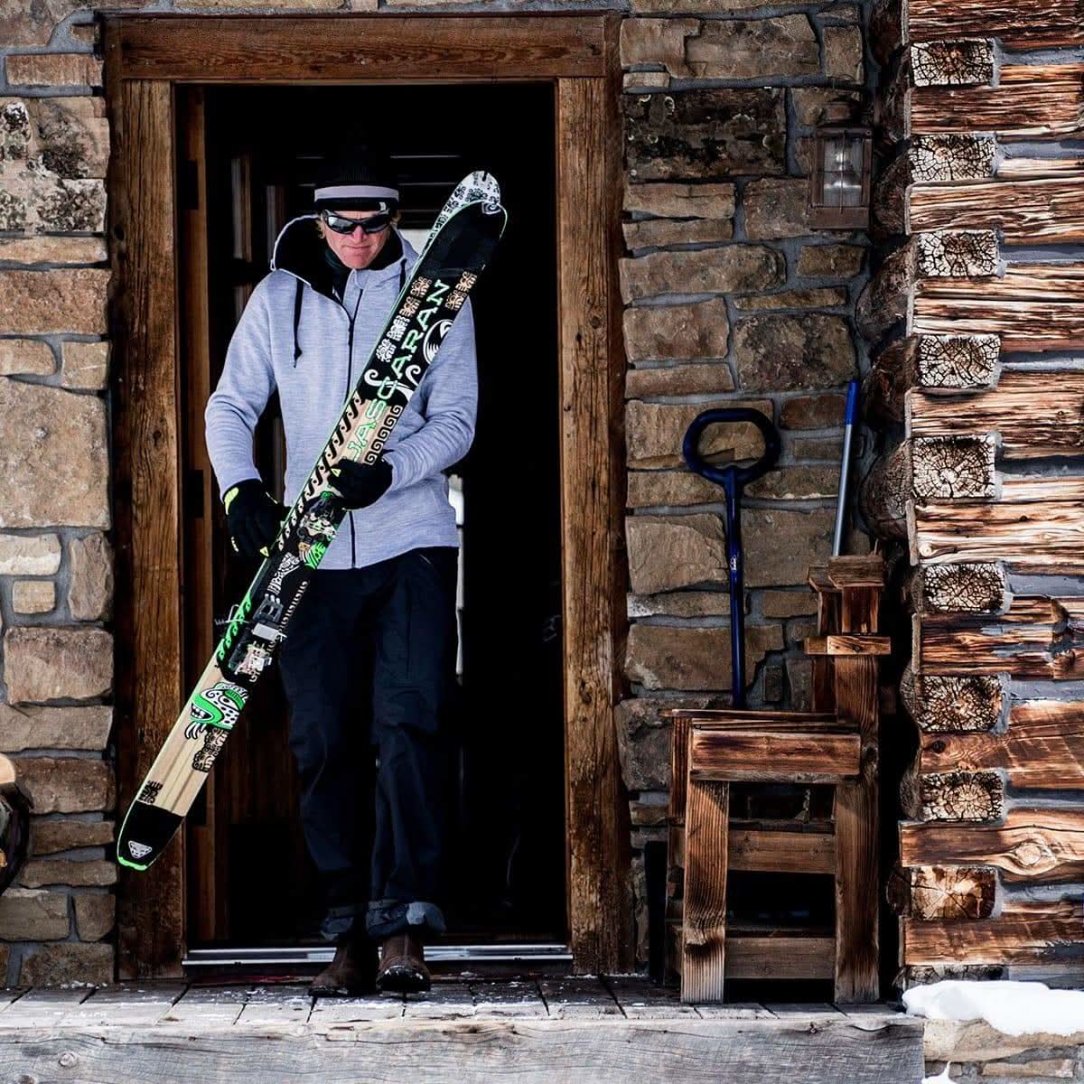 A man comes out of a cabin with skis in hand. The man is modeling the heavyweight brushed wool Kodiak Fleece Hoodie, crafted with thumbholes and a drawstring to bundle you up for wicked cold days!
