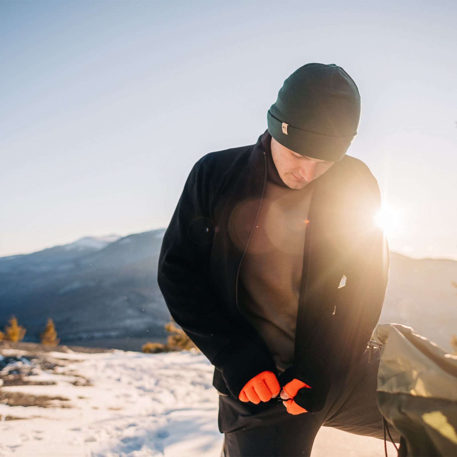 Expedition - Men's Wool Full Zip Wilderness - Minus33 Merino Wool Clothing, man fastening a black full-zip layer at a snowy mountain sunrise
