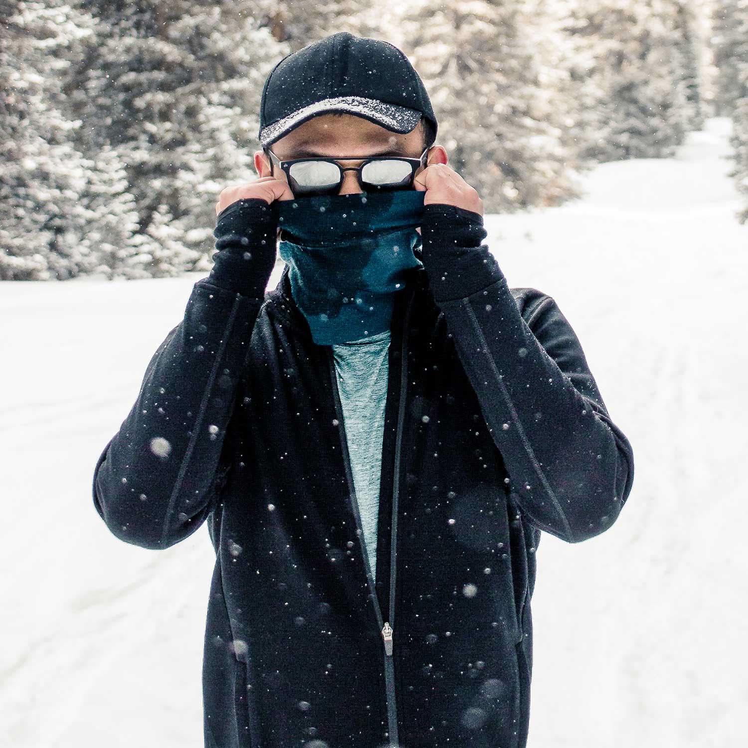 Expedition - Men's Wool Full Zip Wilderness - Minus33 Merino Wool Clothing, man wearing a black full-zip top while pulling up a neck gaiter in falling snow