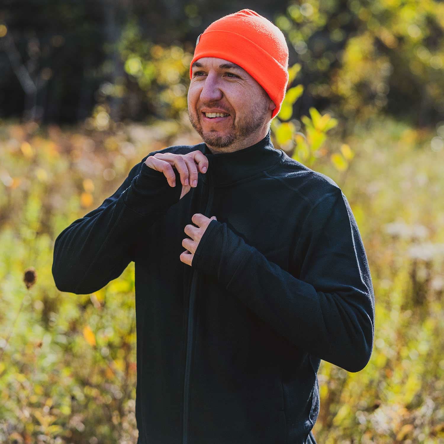 Expedition - Men's Wool Full Zip Wilderness - Minus33 Merino Wool Clothing, man zipping the collar of a black full-zip top in a sunlit field