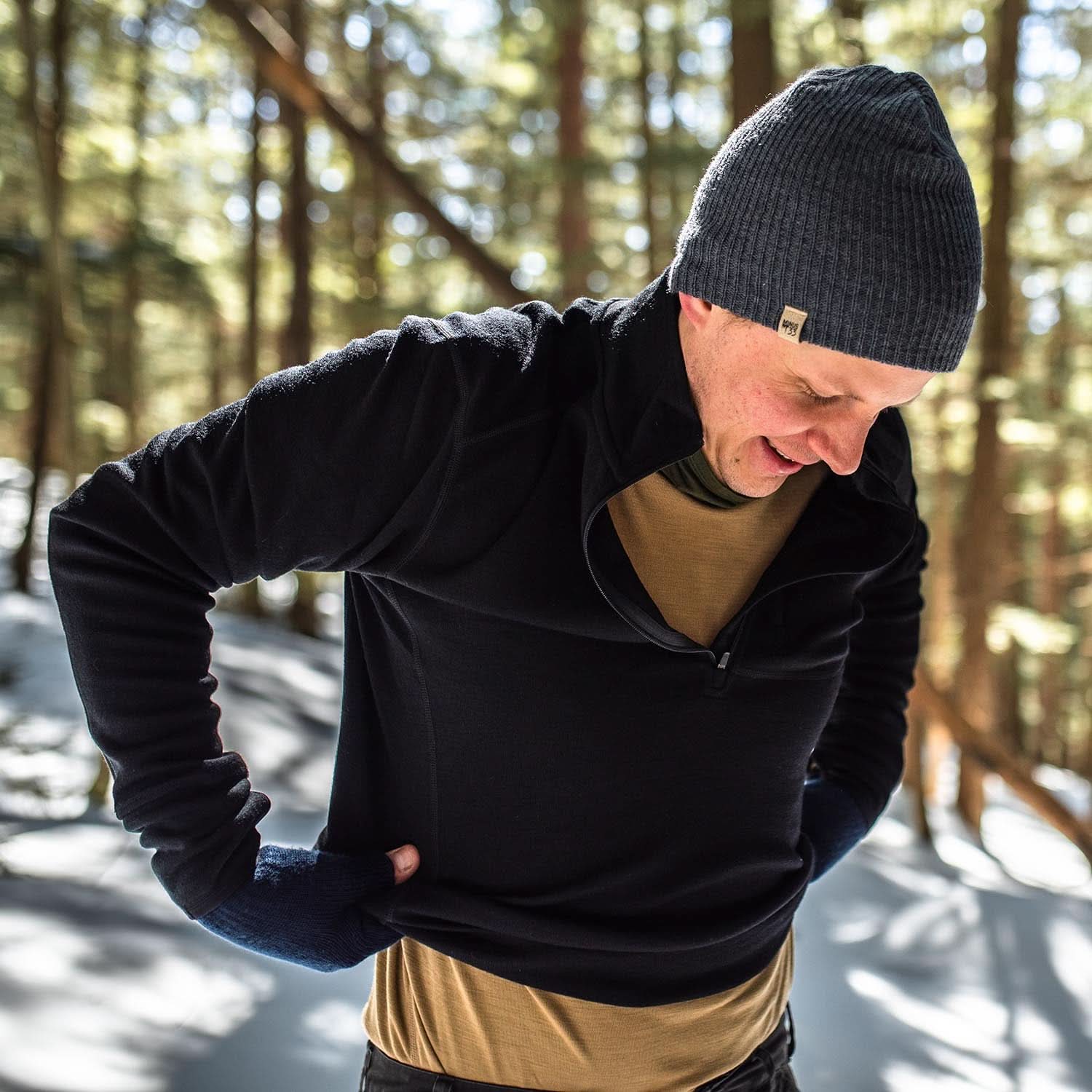 Expedition - Men's Wool 1/4 Zip Wilderness - Minus33 Merino Wool Clothing, man adjusting the hem of a black quarter-zip top in a snowy forest