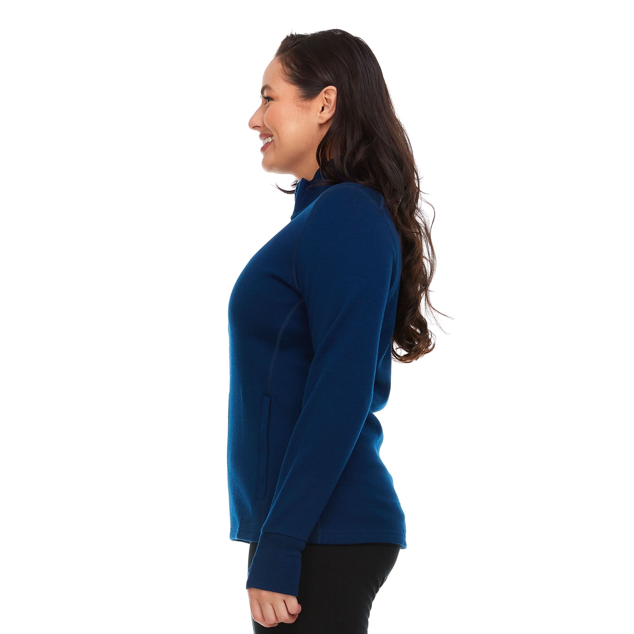 A woman models a hundred percent merino wool heavyweight full zip sweater. This outer layer features a two and a half inch mock neck collar, two zippered pockets, and thumbholes.