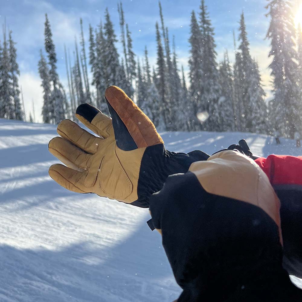 Close-up of gloved hands in a snowy landscape with trees and sunlight. Waterproof winter ski gloves