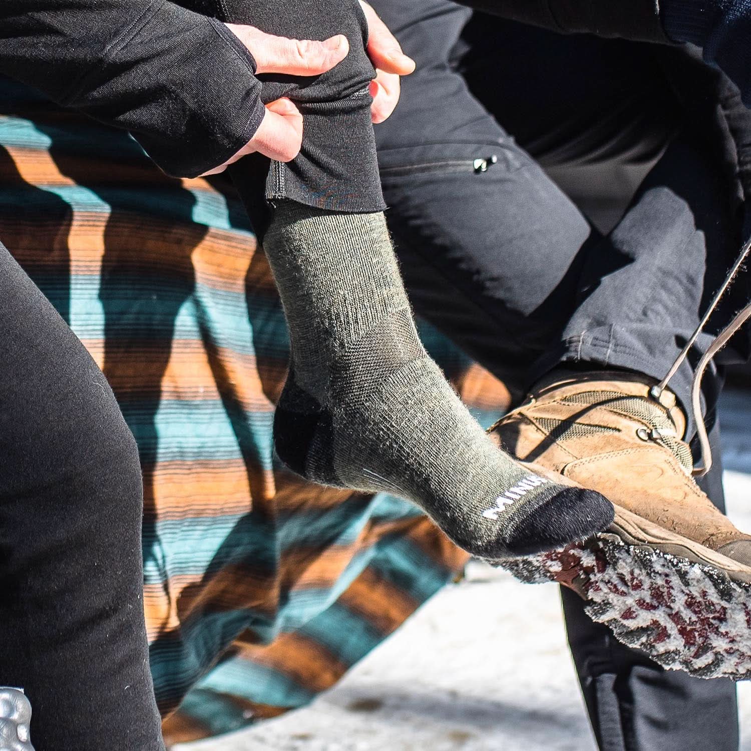Three-quarter lifestyle view of olive drab lightweight cushioned merino wool crew socks being worn, showing ribbed cuffs, fitted ankles, shaped heels, padded footbeds, and reinforced toes
