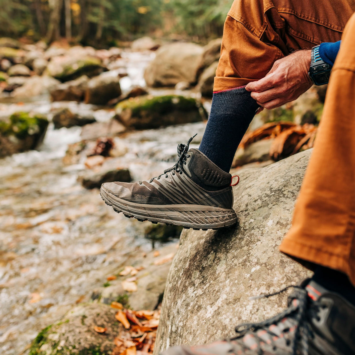 NH USA Made Merino Wool crew socks. Best all season lightweight merino wool crew socks, hiker adjusting sock beside a forest stream
