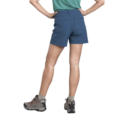 A model from the back wearing a pair of high-waisted, slate blue hiking shorts, paired with hiking boots and a green shirt, against a solid white background.