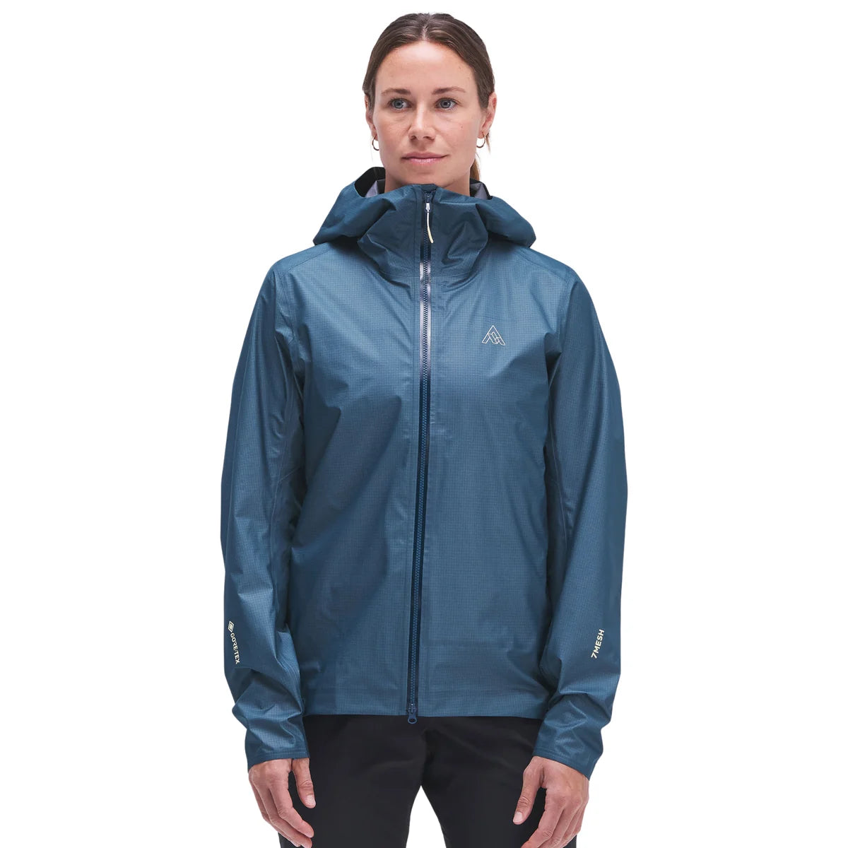 A woman wearing a slate blue hooded waterproof jacket with a full-front zipper and a small white geometric logo on the left chest, set against a plain white background.