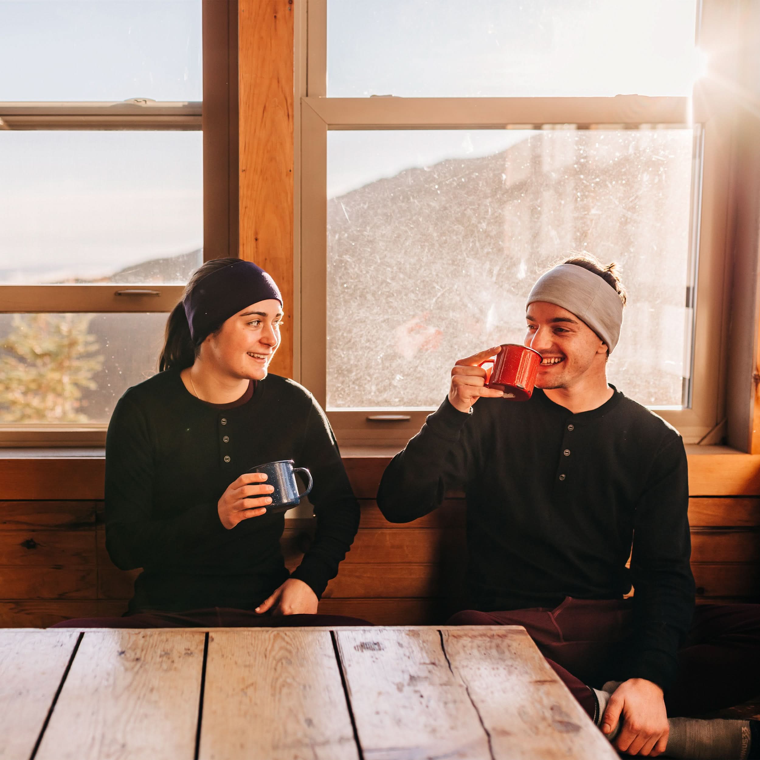 Midweight - Men's Long Sleeve Button Up 100% Merino Wool. Our best-selling Midweight fabric now as a long-sleeve henley. midlayer, two people in henleys drinking from mugs at a cabin table