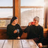 Midweight - Men's Long Sleeve Button Up 100% Merino Wool. Our best-selling Midweight fabric now as a long-sleeve henley. midlayer, two people in henleys drinking from mugs at a cabin table
