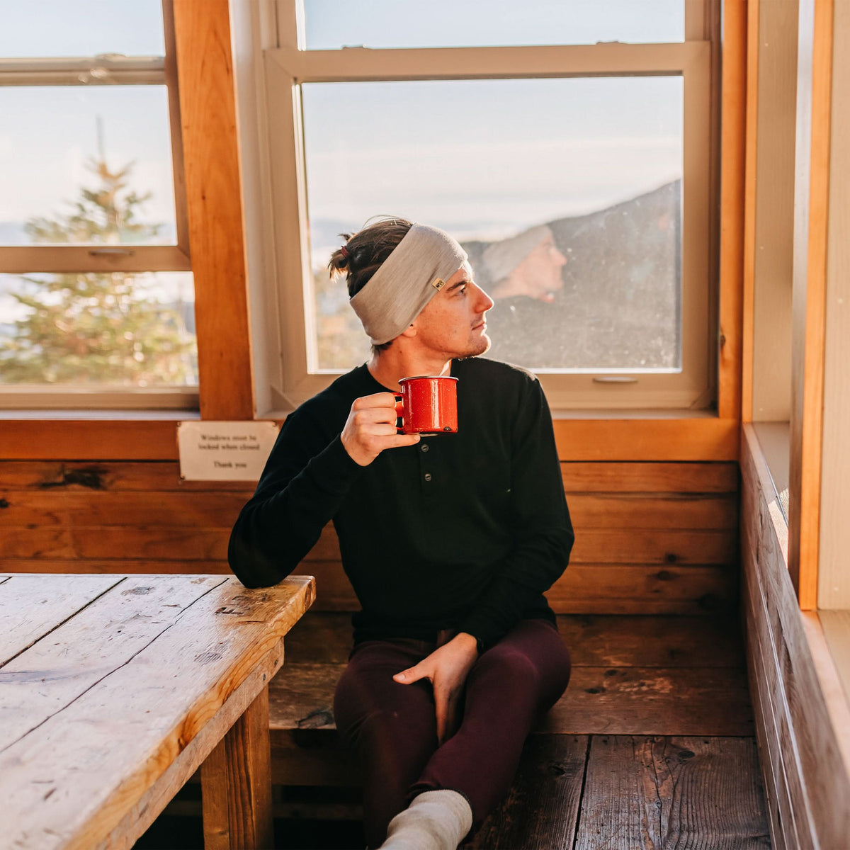Midweight - Men's Long Sleeve Button Up 100% Merino Wool. Our best-selling Midweight fabric now as a long-sleeve henley. midlayer, man seated alone with a red mug beside a cabin window