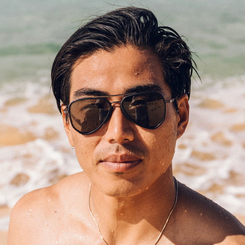 Sunski Astra Polarized Sunglasses - Black Forest - Man wearing sunglasses on a beach with ocean waves in the background