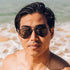 Sunski Astra Polarized Sunglasses - Black Forest - Man wearing sunglasses on a beach with ocean waves in the background
